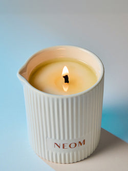 Lit NEOM wellbeing candle in white ceramic vessel creating calming spa atmosphere.