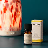 NEOM Happiness Essential Oil Blend with packaging and diffuser on a teal background