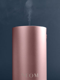 Pink NEOM Pod Mini+ diffuser with steam on a dark background