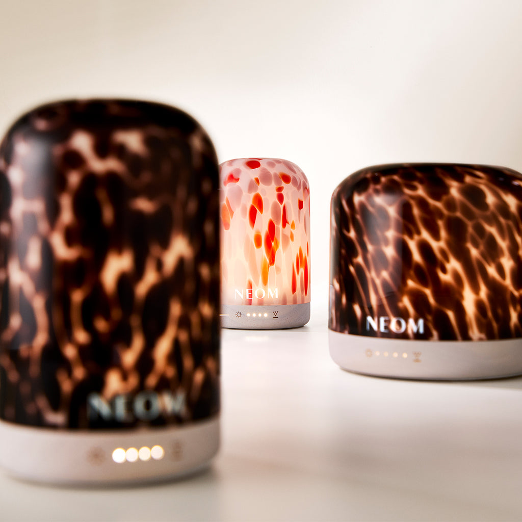 Three NEOM diffusers with clementine and tortoiseshell designs on a light background