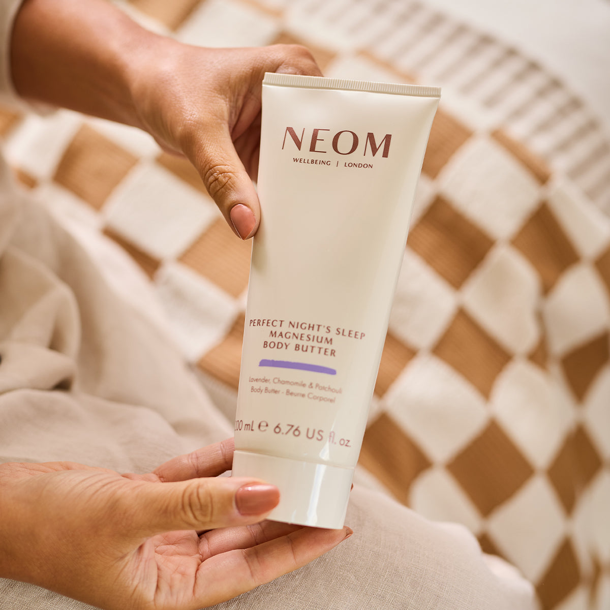 A person holding the NEOM perfect nights sleep magnesium body butter on their bed