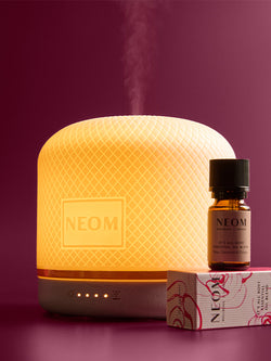 NEOM pod luxe diffuser and essential oil bottle on a purple background