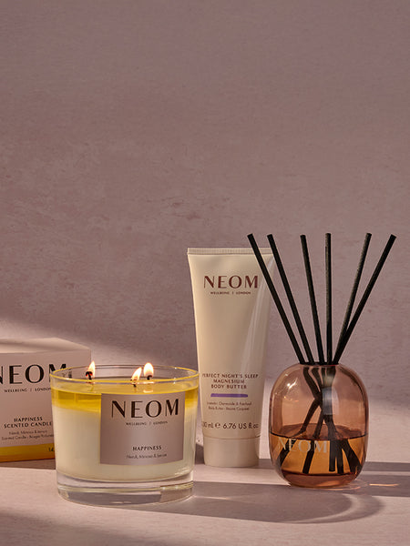 NEOM candle, body butter, and reed diffuser on a neutral background