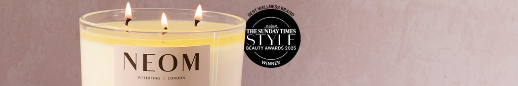NEOM candle with three flames on a plain background, featuring The Sunday Times Style Beauty Awards 2025 winner badge.