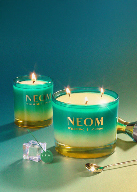 Two NEOM candles on a gradient blue and green background