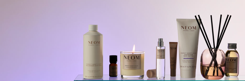 Collection of NEOM products on a shelf with a candle and reed diffuser.