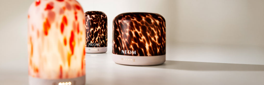 Three NEOM electric diffusers with tortoiseshell and clementine designs on a white surface