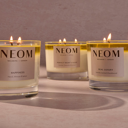 Three NEOM candles with labels on a neutral background