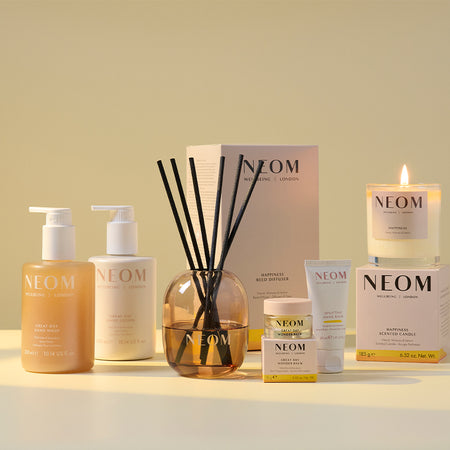 NEOM bath, body and home products; line up including a hand wash and lotion, reed diffuser, wonder balm, a hand balm and candle on a light background