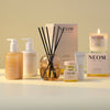 NEOM bath, body and home products; line up including a hand wash and lotion, reed diffuser, wonder balm, a hand balm and candle on a light background