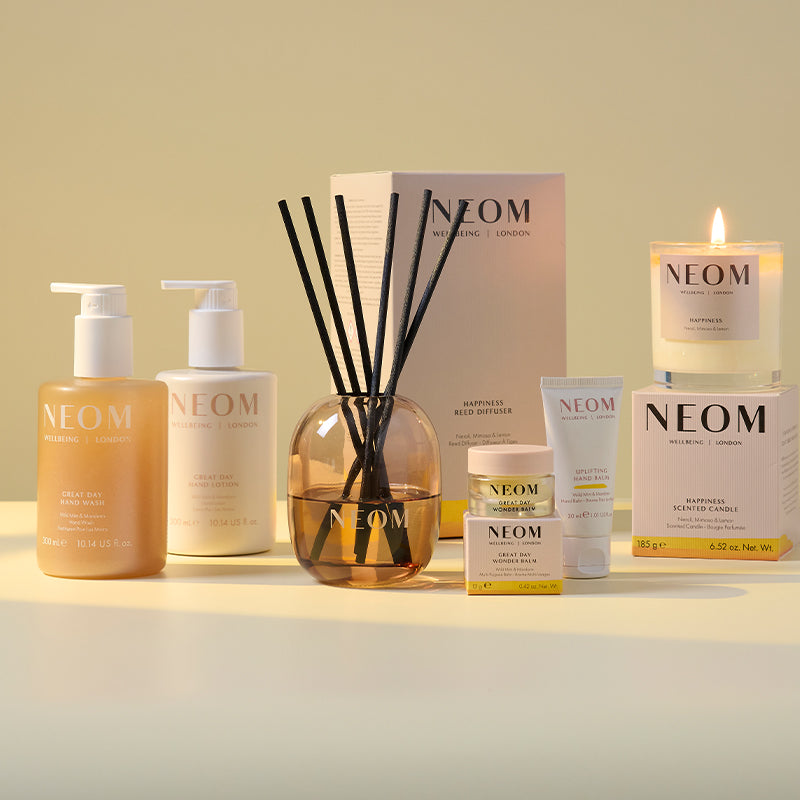 NEOM bath, body and home products; line up including a hand wash and lotion, reed diffuser, wonder balm, a hand balm and candle on a light background
