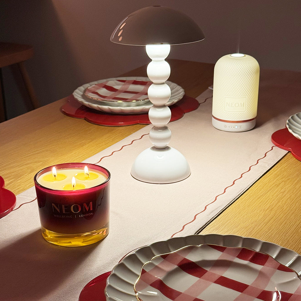NEOM candle and diffuser on a table with checkered plates and a lamp.