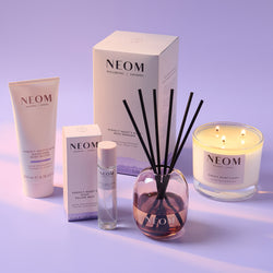 NEOM product range including a candle, reed diffuser, and other items on a light purple background