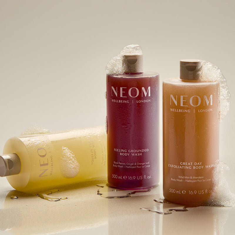 three NEOM body washes in fragrances feeling grounded, great day and squeeze the day on a shelf 
