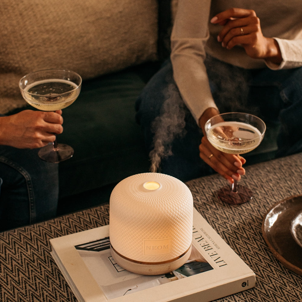 Two people sitting on a couch holding glasses of champagne with a diffuser emitting steam.