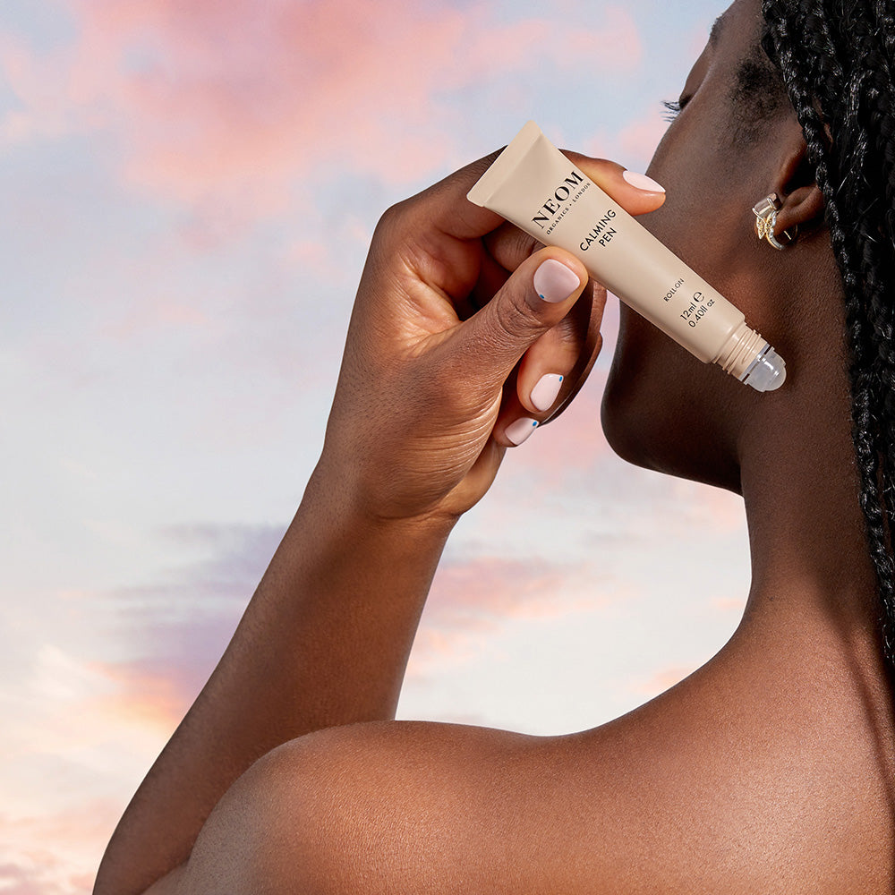 Person applying a calming pen with a blurred sky background