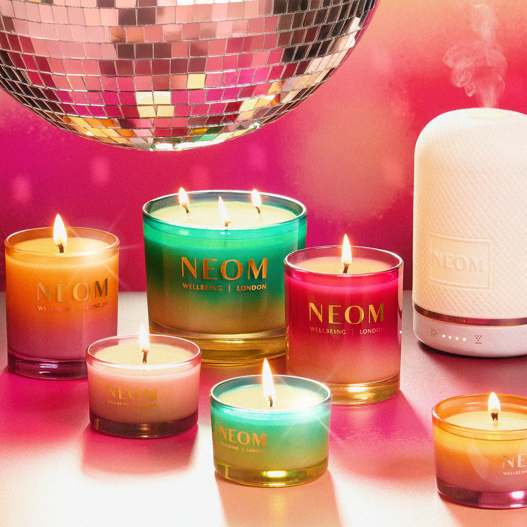 NEOM candles and diffuser on a reflective surface with a disco ball in the background