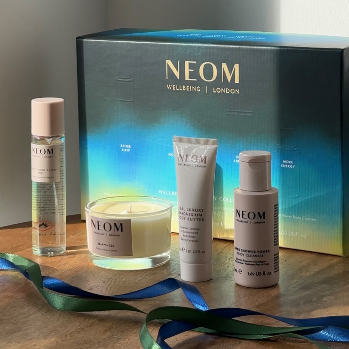 NEOM Wellbeing Discovery Collection gift set with candle, body butter, cleanser, and spray on wooden surface.
