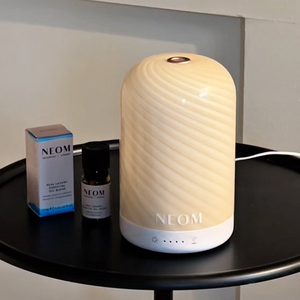 NEOM cinnamon swirl pod diffuser in a bedroom with an essential oil blend