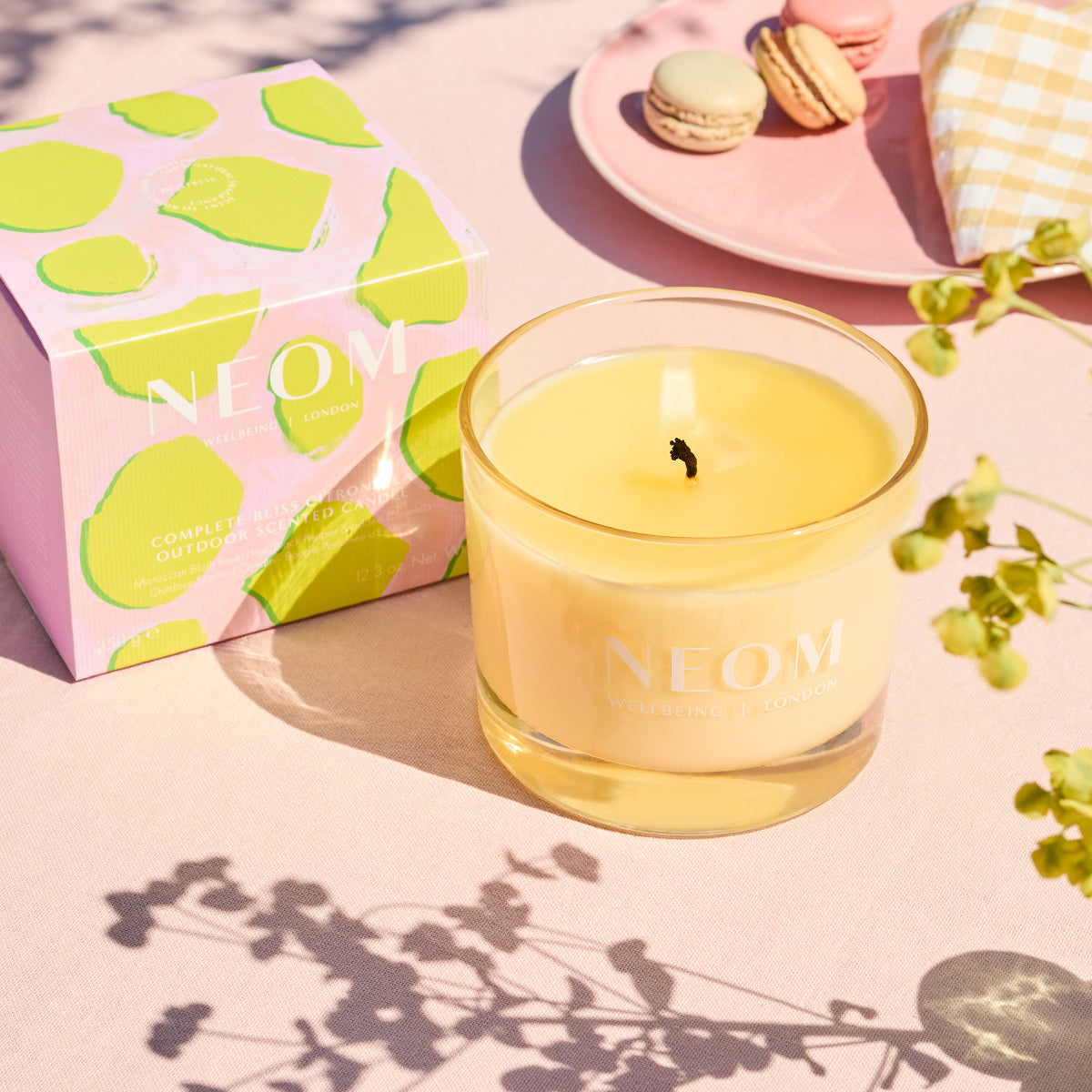 Neom candle with a pink box featuring green lime illustrations on a light pink surface.