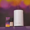 NEOM diffuser, essential oil blend, and oil bottle on a purple background