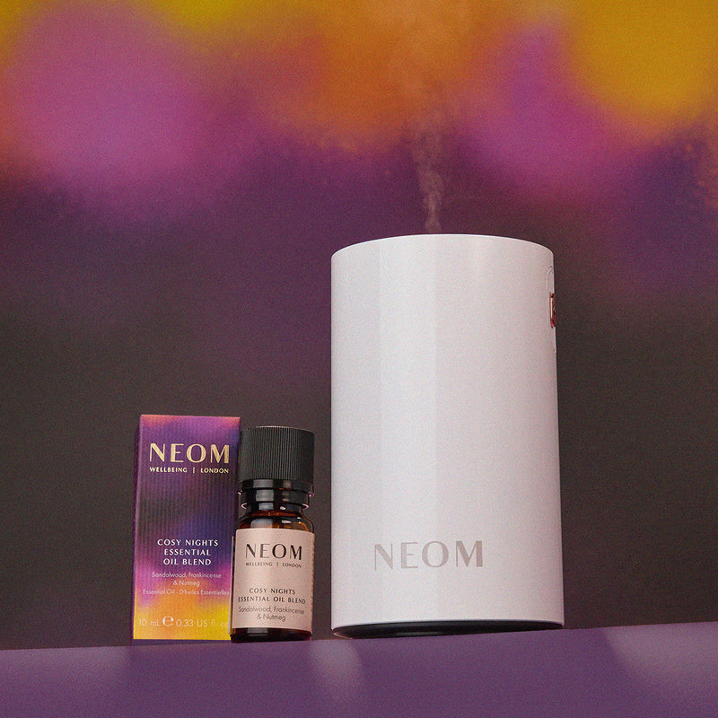 NEOM diffuser, essential oil blend, and oil bottle on a purple background