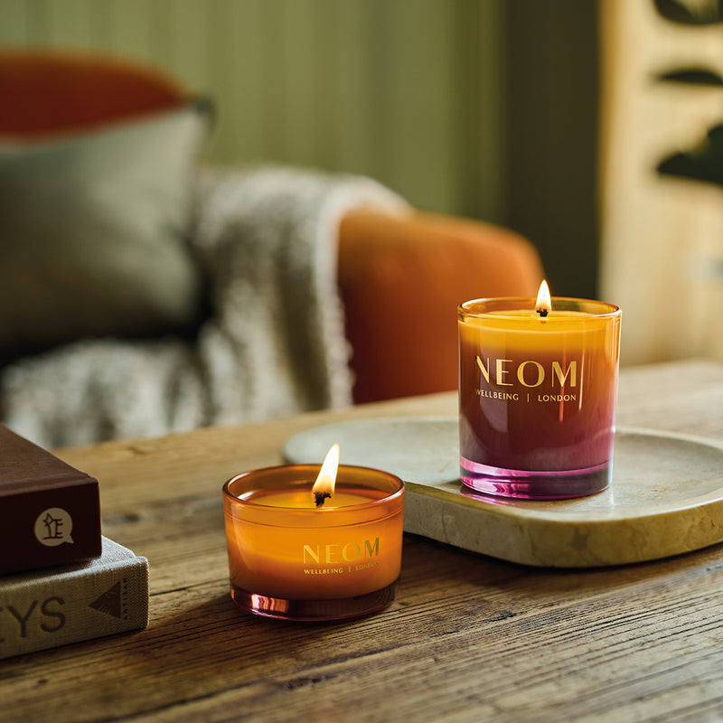 Two NEOM Cosy Night's candles on a wooden surface with a blurred background
