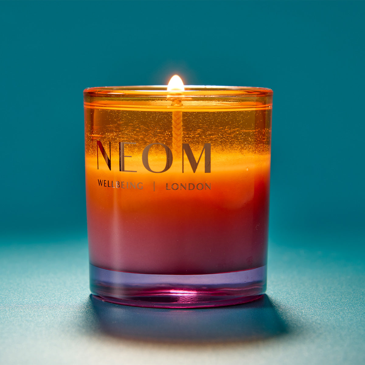 NEOM candle with a gradient colour on a blue background
