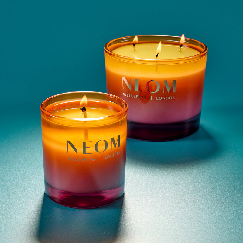 Two NEOM candles with a gradient color scheme on a blue background