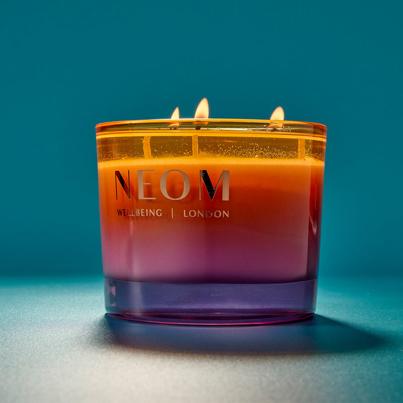 NEOM candle with a gradient color on a blue background