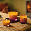 Three NEOM Cosy Night's candles on a wooden surface with a warm glow.