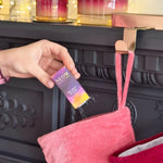 Person placing NEOM Cosy Nights Essential Oil Blend box into pink Christmas stocking on decorated mantel.