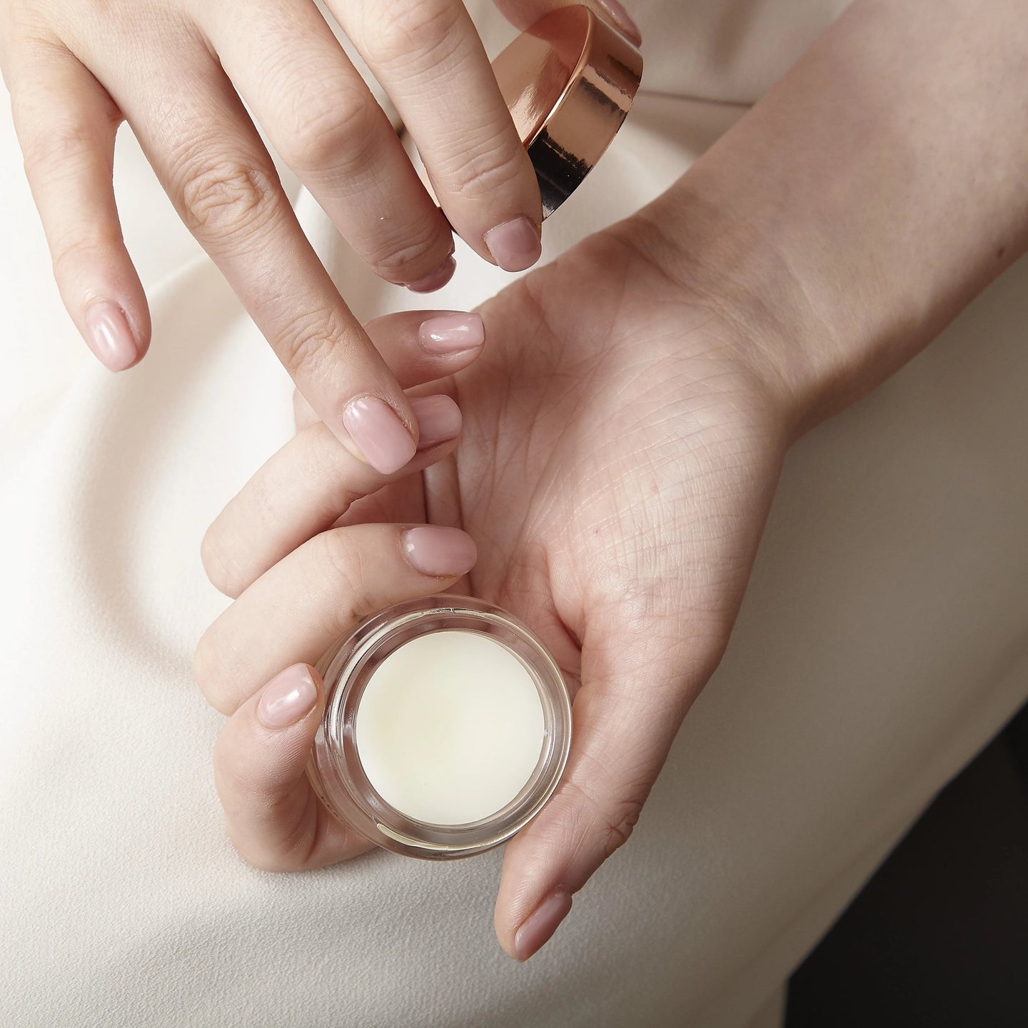 Close-up of hands holding the NEOM wonder balm with a beige background