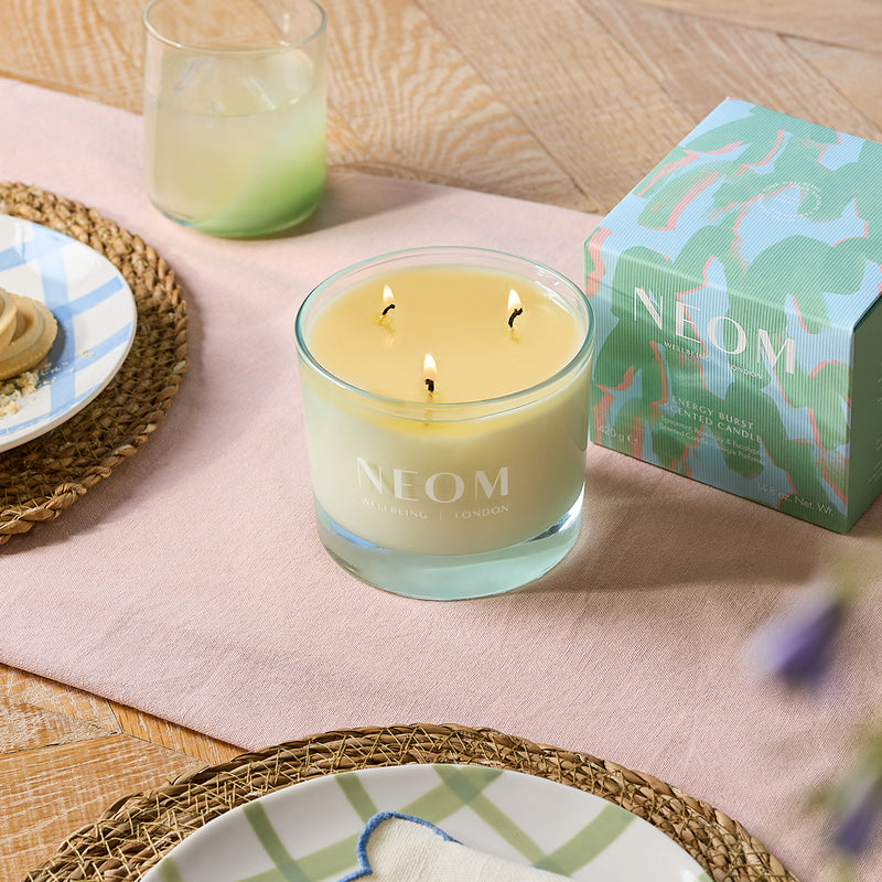 Neom candle with packaging on a table with plates and glasses