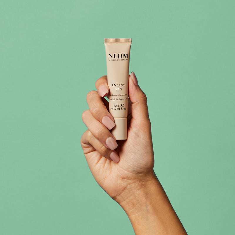 Hand holding a NEOM Energy Pen against a green background