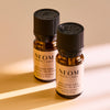 Two NEOM Feel Good Vibes essential oil blend bottles standing on a surface with soft shadows.