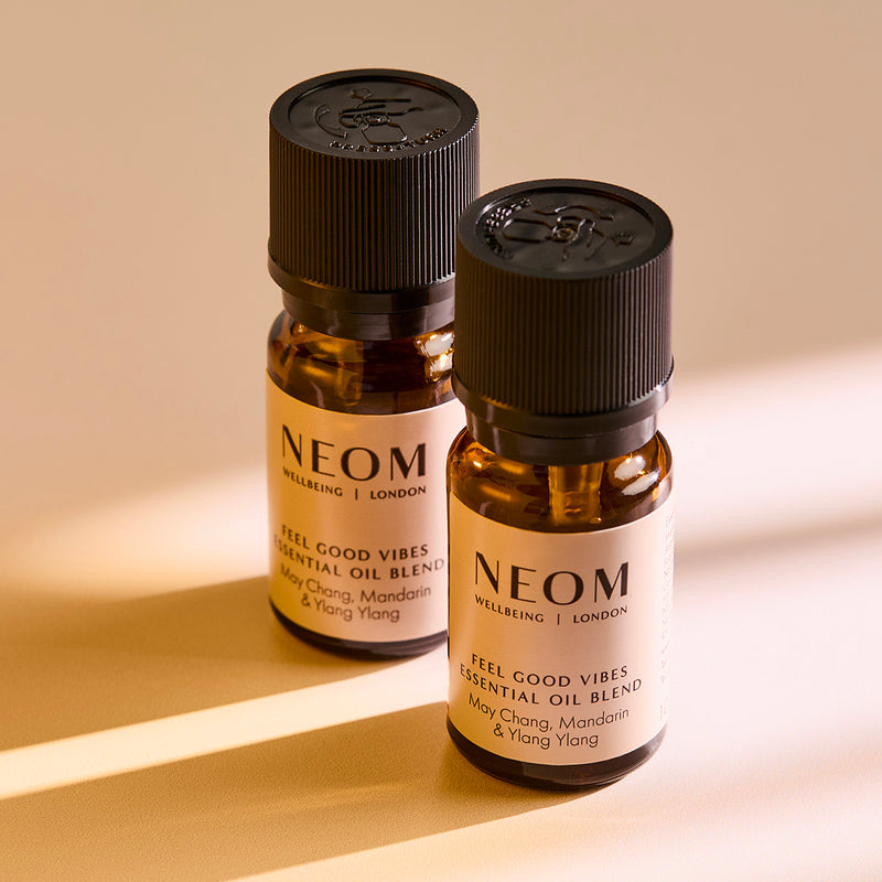 Two NEOM Feel Good Vibes essential oil blend bottles standing on a surface with soft shadows.