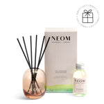 NEOM  diffuser set with rose gold diffuser, black reeds, and small bottle on a white background.
