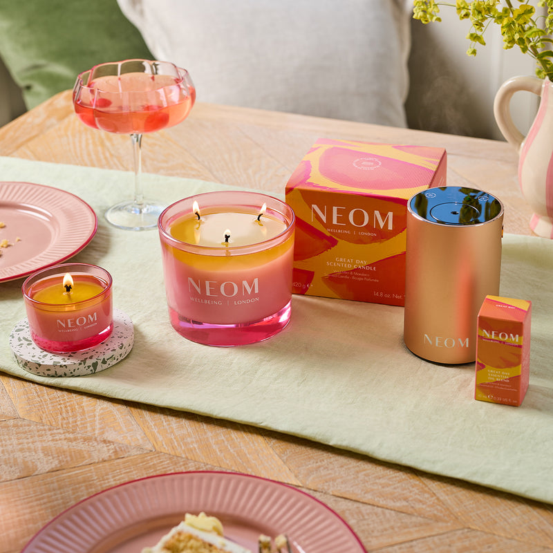 Neom candles and products on a table with a glass of pink drink and plates.