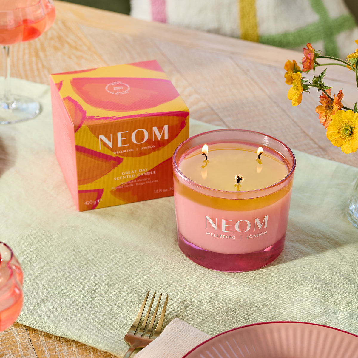 NEOM candle on a table with a box and flowers in the background