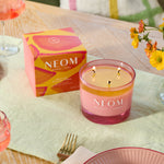 NEOM candle on a table with a box and flowers in the background