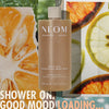 “NEOM Great Day Exfoliating Body Wash (500 ml) centered over a collage of citrus slices and greenery. Text reads: ‘Shower on. Good mood loading…’”