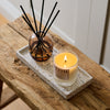 NEOM Real Luxury scented candle and reed diffuser displayed together on a black tray on a rustic wooden bench.
