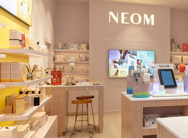 NEOM store interior with shelves displaying products and a digital display.