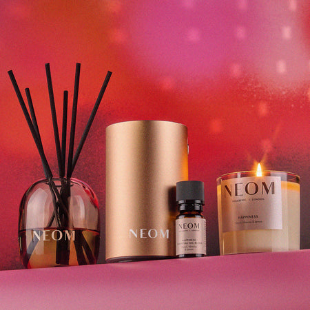 NEOM product set including a candle, diffuser, and essential oil on a pink background