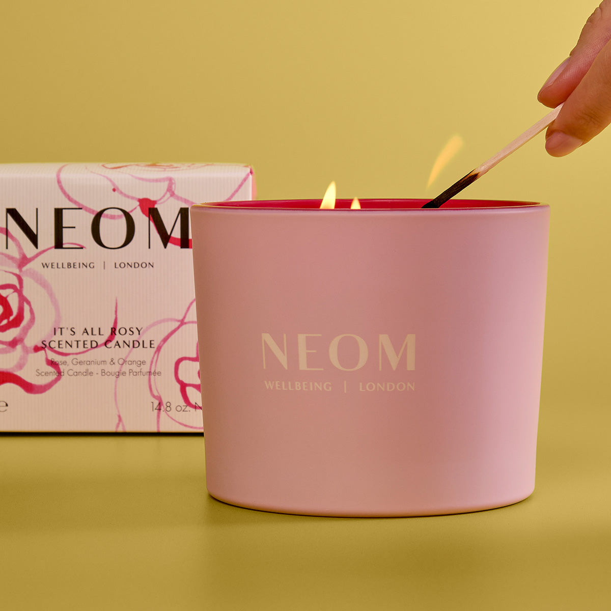 NEOM candle being lit with a box in the background on a yellow background