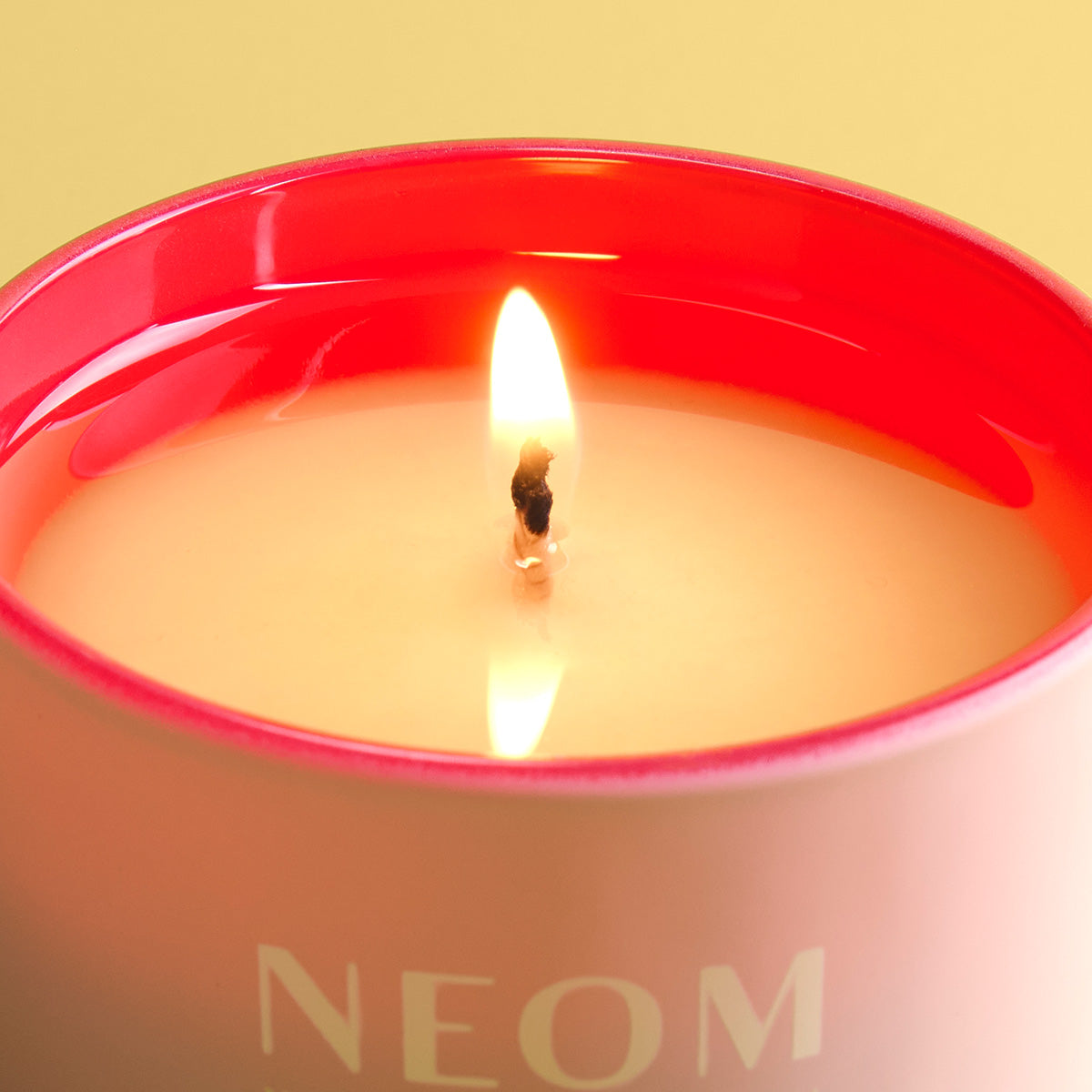 NEOM candle with flame on a yellow background