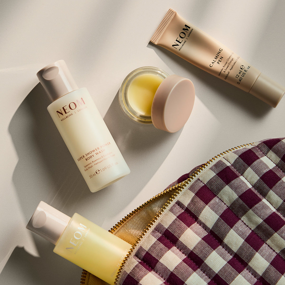 Flat lay of an open bag with NEOM products including Squeeze the Day Body Wash, super shower power body wash, wonder balm