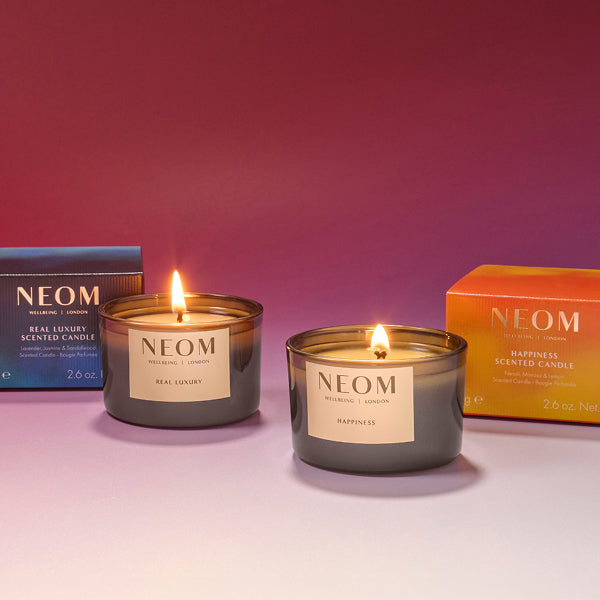 NEOM limited-edition Real Luxury and Happiness scented travel candles with packaging on a gradient background