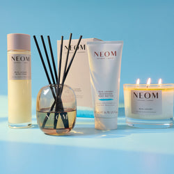 NEOM product lineup including bottle, reed diffuser, and candle on a blue background
